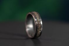 a wedding band with gold glitter inlays sits on a black surface, ready to be used as a ring