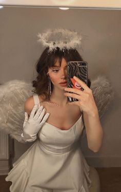 a woman dressed in white taking a selfie with an angel wings on her head