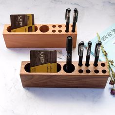 several pens and pencils in wooden holders on a marble counter top with a book