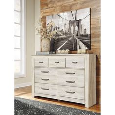 a white dresser with drawers in front of a wooden wall and painting on the wall