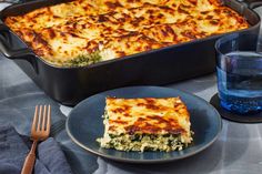 a casserole dish with cheese and spinach on a plate next to a glass of water