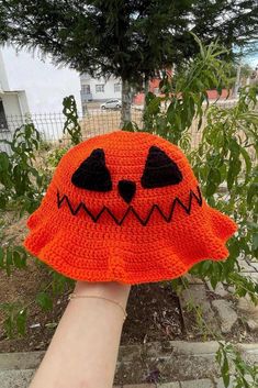 a hand is holding an orange knitted hat with black eyes and teeth on it