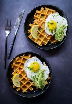 two black plates topped with waffles and fried eggs