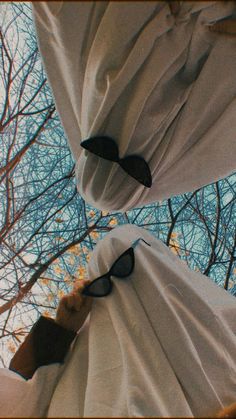 the view from below looking up at trees with white sheets covering them and black sunglasses