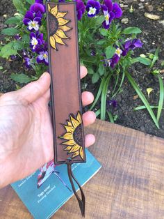 a hand holding a bookmark with flowers in the background