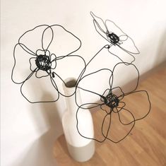 three wire flowers in a white vase on a wooden floor next to a white wall