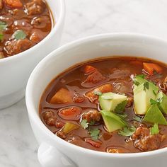 two white bowls filled with meat and vegetable soup on top of a marble countertop