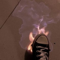 a person's black sneakers with white laces on them are standing in front of a fire