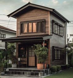 the house is made out of wood and has plants in pots on the front porch