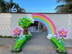 an arch decorated with balloons and flowers in front of a white wall on the street