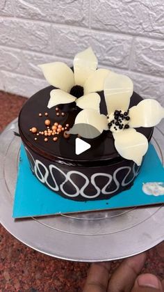 a chocolate cake with white flowers on top is being held up by someone's hand