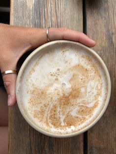 a person holding a cup of coffee on top of a wooden table