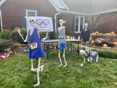 three skeleton statues in front of a house decorated for the olympics with flags and balloons