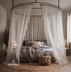 a canopy bed with sheer curtains and pillows in the middle of a wooden floored room