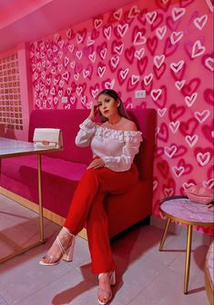 a woman sitting on top of a red couch in front of a wall with hearts