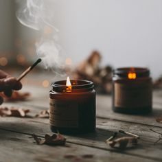 a person lighting a candle with a stick in front of it on a wooden table