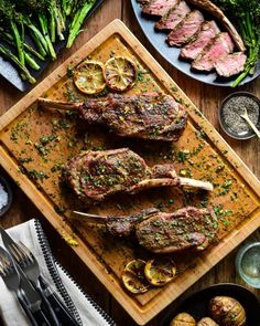 a wooden cutting board topped with meat next to broccoli and lemon wedges