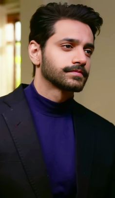 a man with a goatee wearing a blue turtle neck shirt and black blazer