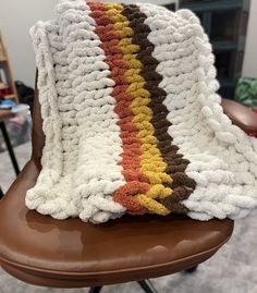 a crocheted blanket sitting on top of a brown chair next to a table