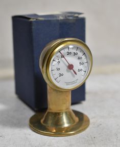 a brass clock sitting on top of a table next to a blue box with a red needle