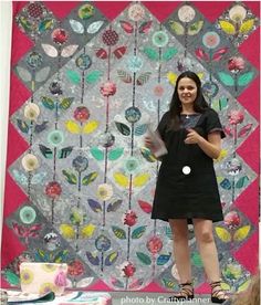 a woman is standing in front of a quilt