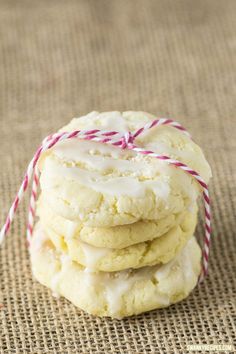 a stack of cookies with white icing and red twine on the top, sitting on a burlap surface