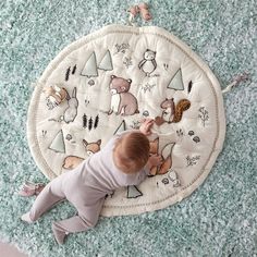 a baby laying on the floor playing with a rug that has animals and trees on it