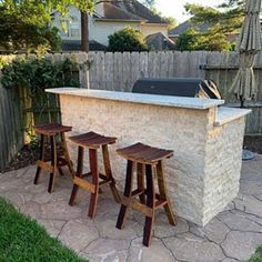 an outdoor kitchen with three stools in front of it and a grill on the back