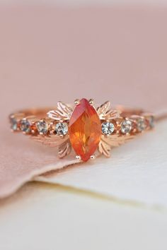 an orange and white diamond ring sitting on top of a pink napkin with gold accents