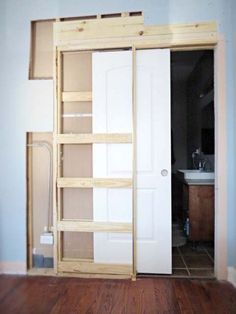 an empty room with wooden floors and white closet doors in the center, open to reveal a bathroom