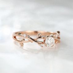 a rose gold ring with an oval cut diamond in the center and leaves on each band