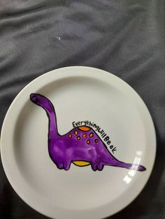 a white plate with a purple dinosaur painted on it's side and the words, everything is real