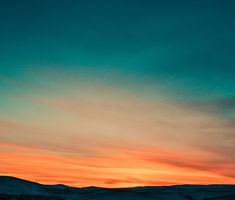 an orange and blue sky at sunset with mountains in the background