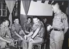 black and white photograph of men in uniform talking to each other while sitting on chairs