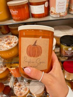 a woman holding up a jar of pumpkin spice in front of shelves filled with jars