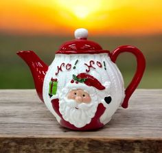 a red and white teapot with santa clause on it's side sitting on a wooden table