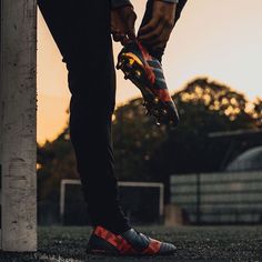 a person standing on top of a field holding onto a soccer shoe with the sun setting in the background