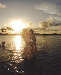 two women standing in the water with their arms around each other as the sun sets