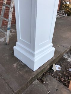 a tall white pillar sitting on the side of a street next to a sidewalk with a ladder