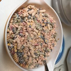 a white bowl filled with pasta salad on top of a counter next to silverware