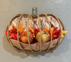 three pumpkins in a woven basket with autumn leaves on the top and below them