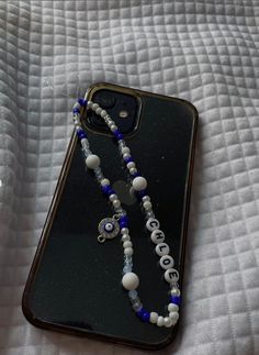 a cell phone with a beaded necklace attached to it's back case on a bed