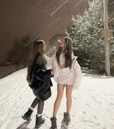 two girls are standing in the snow with their arms around each other as they look up into the sky