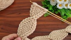 someone is knitting something with yarn on the table next to some flowers and plants in the background