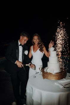 a bride and groom cutting their wedding cake with sparklers in the air behind them