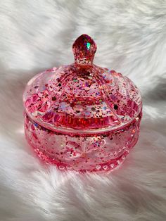 a pink glass covered jar sitting on top of a white fur