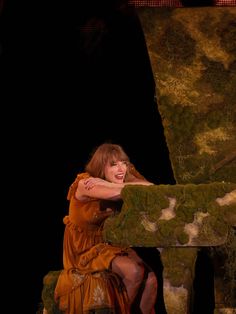 a woman in an orange dress sitting on a moss covered bench with her arms crossed