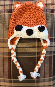 an orange and white knitted animal hat on top of a plaid couch with black eyes