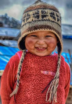 a young child wearing a knitted hat and red sweater with braids smiles at the camera