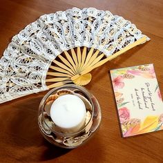 a table topped with a candle and a card next to a decorative fan on top of a wooden table